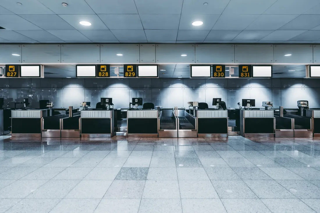 An empty row of airport check-in counters with numbered signs above them and a polished stone floor, typical of buildings served by warehouse cleaning services in San Bernardino County