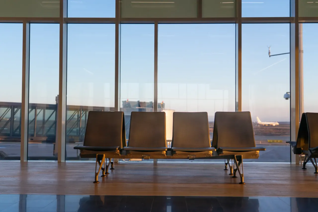 A row of empty black gate seats in front of floor-to-ceiling windows with an aircraft visible on the apron, typical of the facilities covered by airport and aviation cleaning in San Diego County