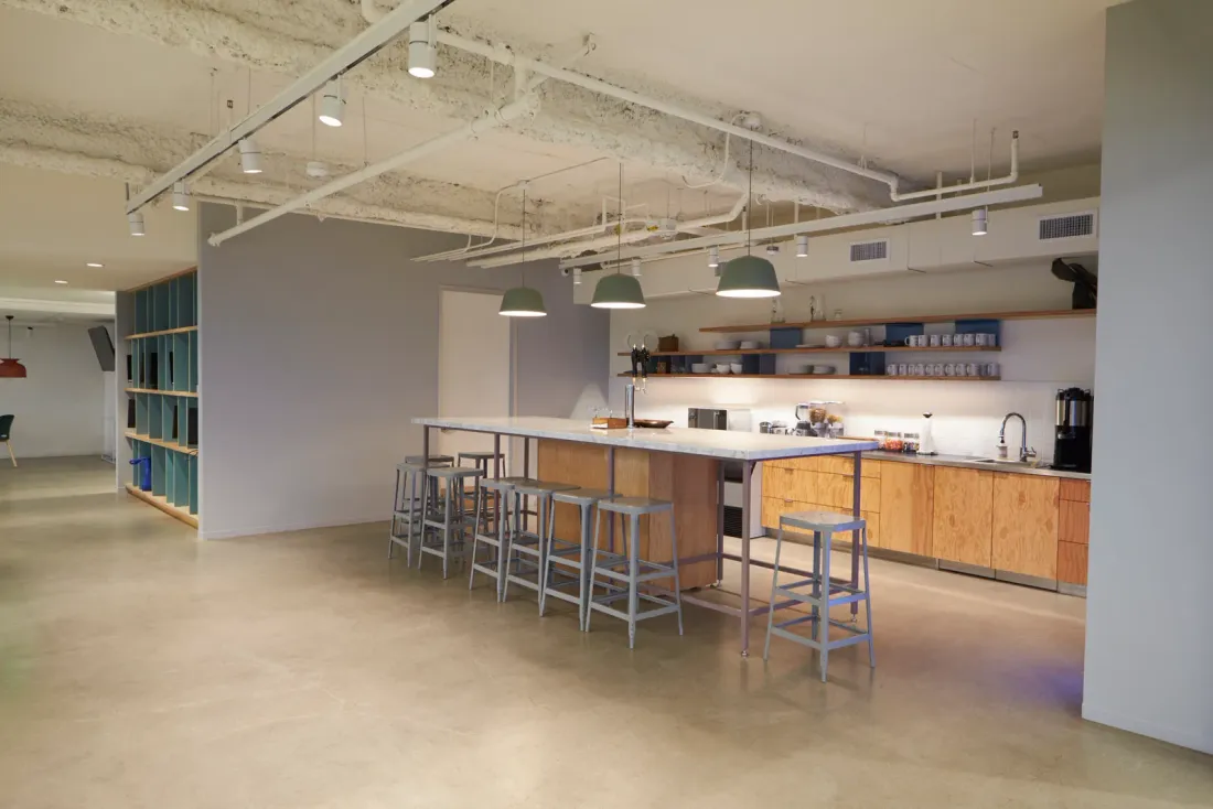 An empty office kitchen with a long island, metal stools, open shelving and a polished concrete floor, typical of buildings on a recurring janitorial program in Paramount, CA