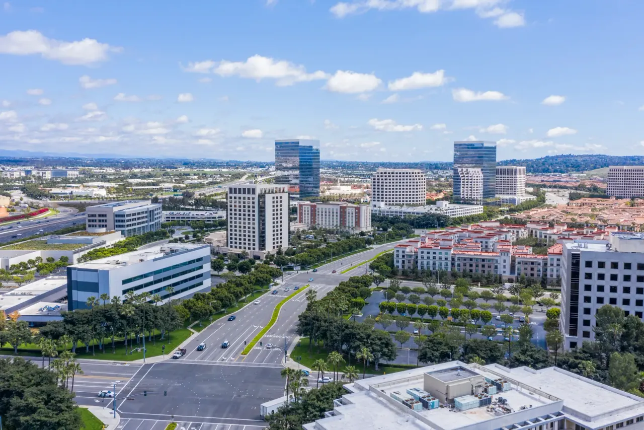 An aerial view of mid-rise office towers, low campus buildings, wide boulevards and trees under a blue sky with scattered clouds, illustrating commercial cleaning services in Santa Ana, CA