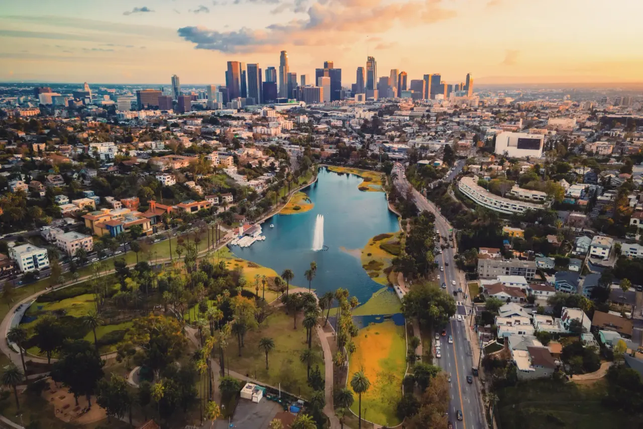 An aerial view over a park with a lake and fountain toward a cluster of downtown towers at sunset, for a page on commercial cleaning services in Glendale, CA