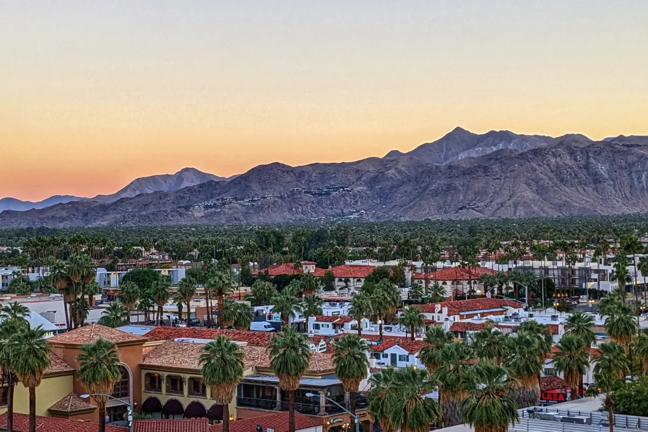 Red-tile rooftops and palm trees below a rugged mountain range in early evening light, related to commercial cleaning services in Palm Springs, CA