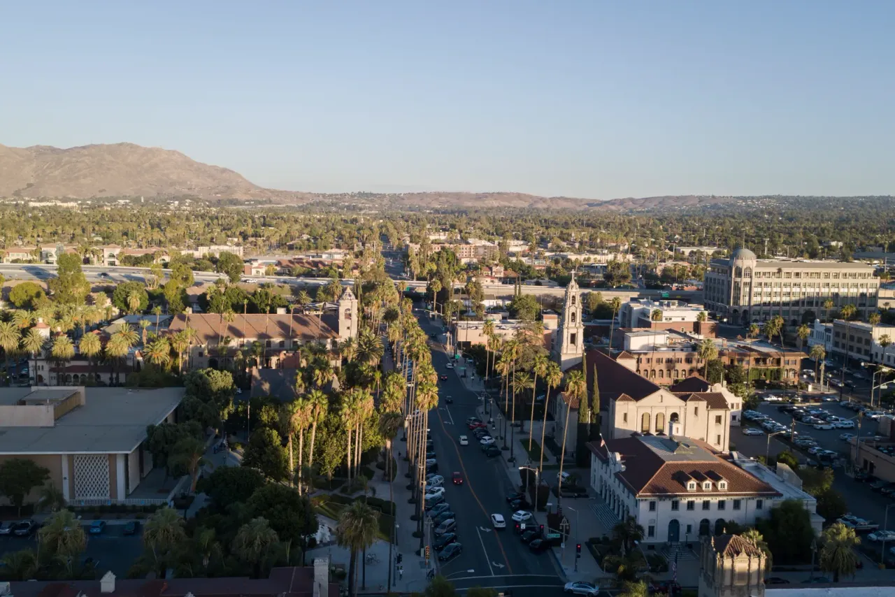 An aerial view of a palm-lined downtown street with low historic buildings and a bell tower, with hills on the horizon, related to commercial cleaning services in Riverside, CA