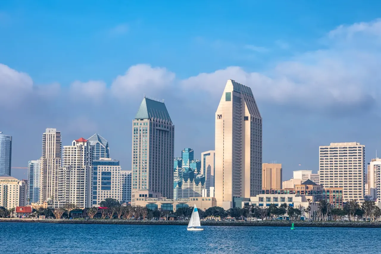 A downtown skyline of high-rise towers across a bay, with a small sailboat on the water, related to commercial cleaning services in San Diego, CA