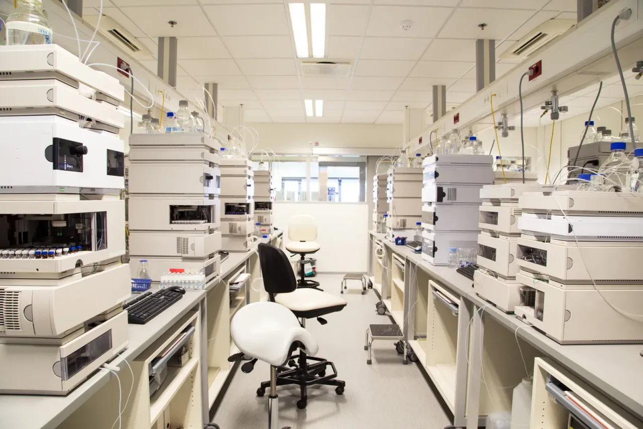 A laboratory with benches of white analytical instruments, monitors and lab chairs under fluorescent lights, an example of the spaces EBS cleans for this sector in San Bernardino County