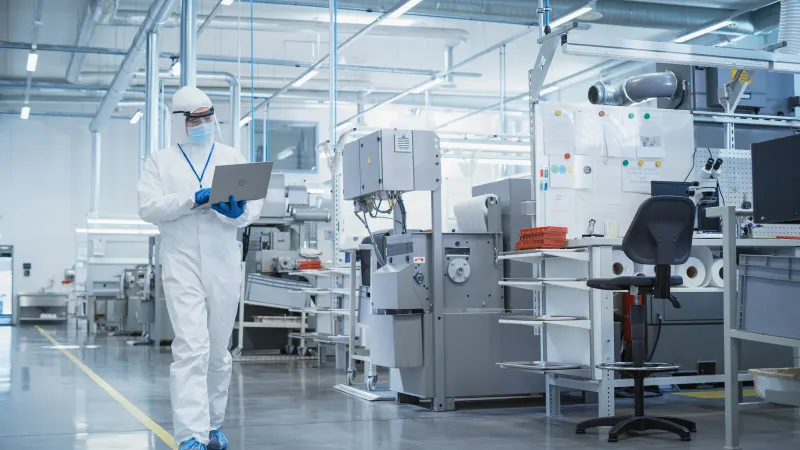 A technician in a sterile coverall walking through a bright, modern manufacturing cleanroom