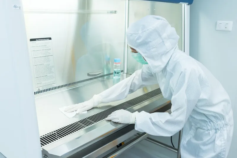A technician in a sterile gown wiping a biological safety cabinet in a cleanroom
