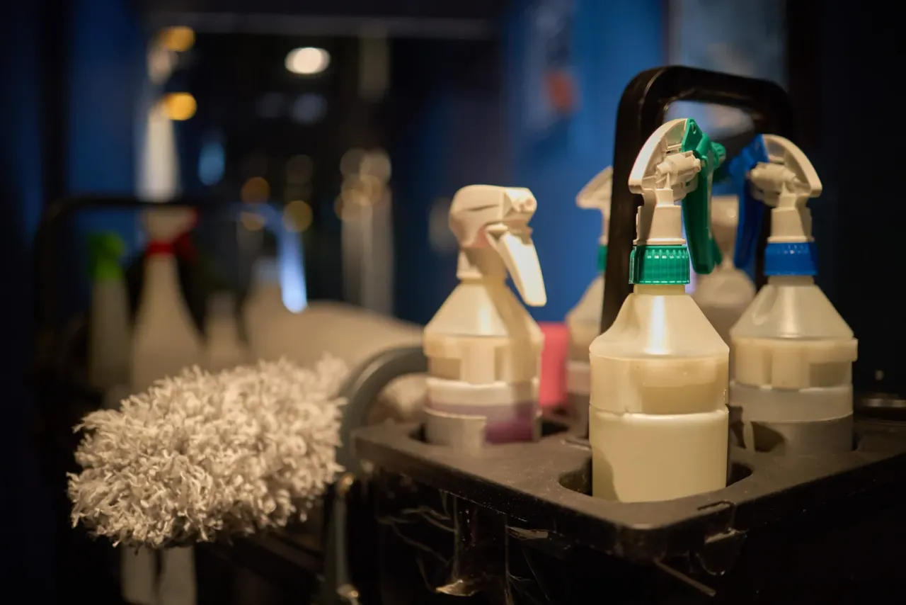 Spray bottles and a duster standing in a cleaning caddy in a dim room, illustrating day porter services in Anaheim, CA