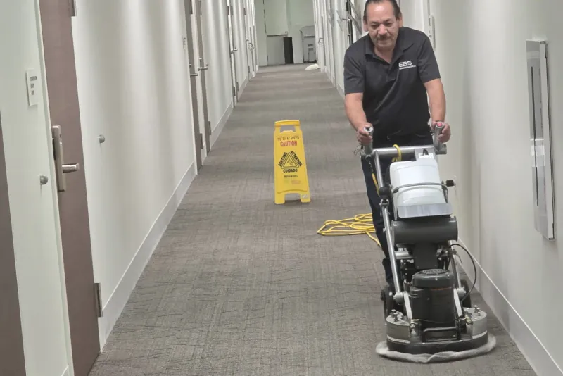 An EBS technician running a carpet cleaning machine down an office corridor
