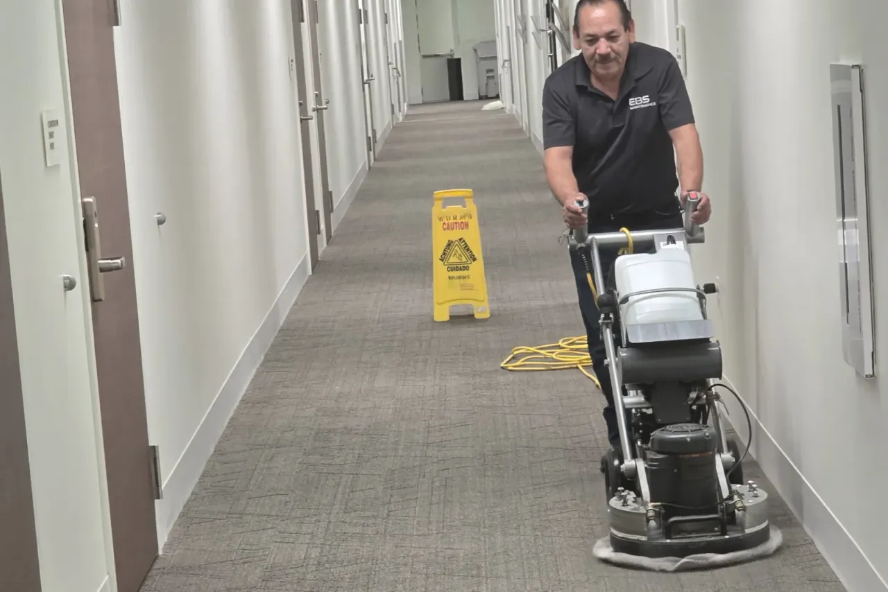 An EBS technician running a carpet cleaning machine down an office corridor