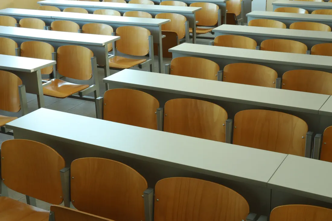 Rows of grey desks with wooden folding seats in an empty lecture hall, a setting for commercial cleaning services in Cypress, CA