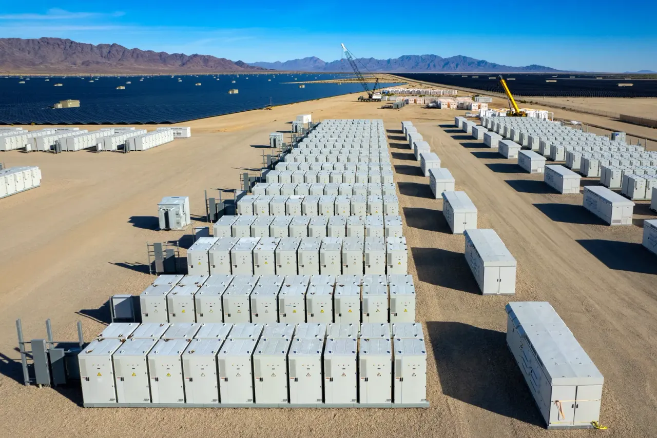 Rows of white battery storage containers on cleared desert ground, with solar panels and mountains beyond, an example of the spaces EBS cleans for this sector in Riverside County