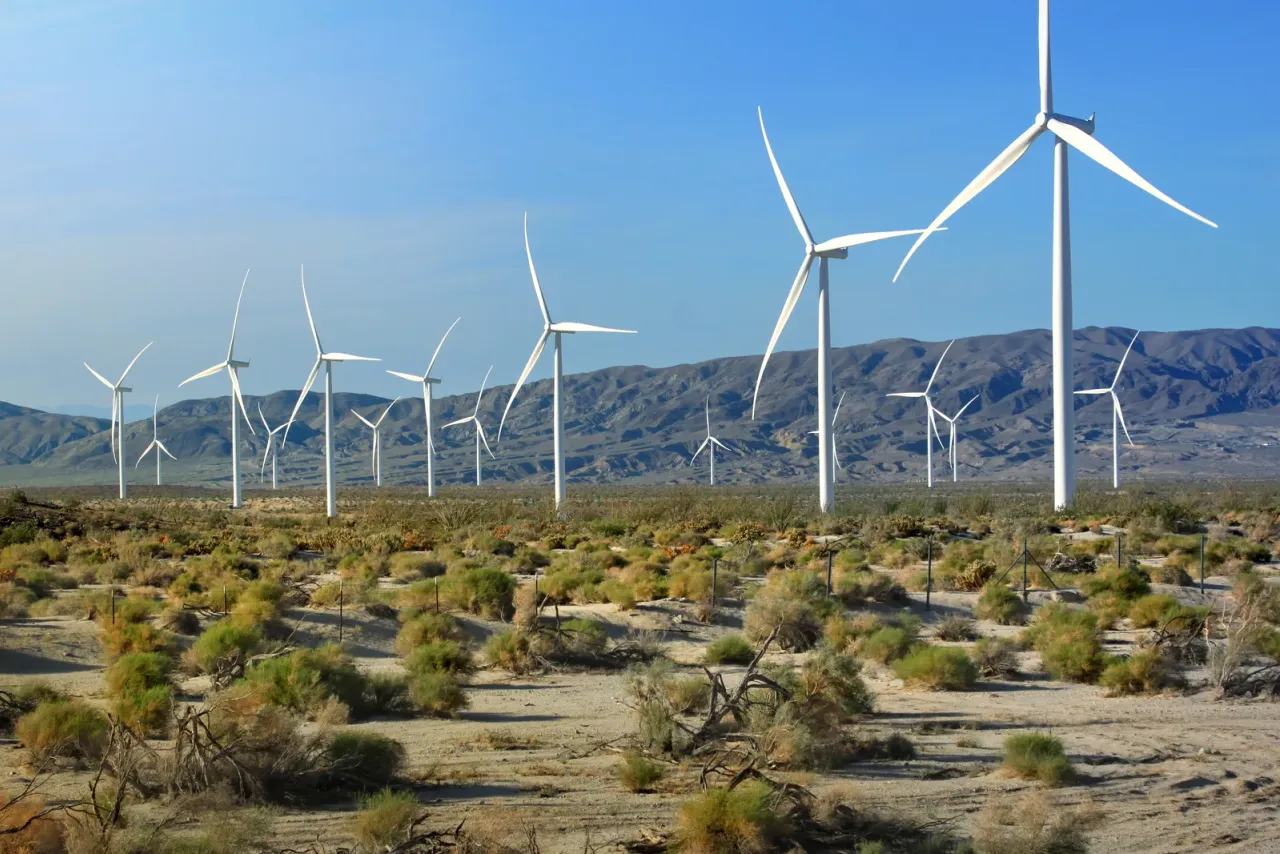 Wind turbines standing among desert scrub in front of a mountain range, illustrating energy and utility facility cleaning in San Bernardino County