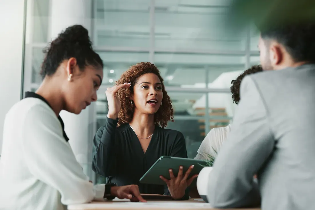 Three people talking around a table with a tablet in a bright, glass-walled office, like the offices EBS cleans for tenants in El Monte, CA