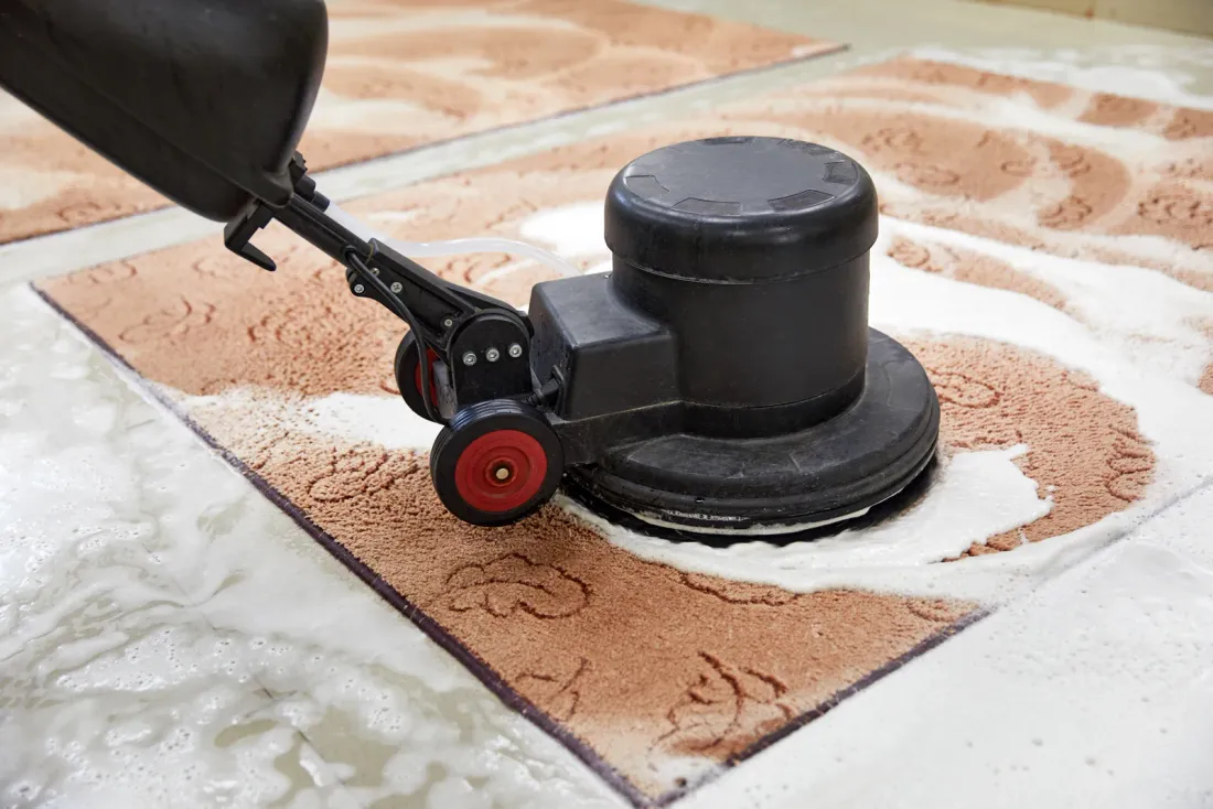 A rotary disc machine scrubbing foam into a terracotta-patterned rug laid on a tile floor, for a page on janitorial services in Whittier, CA
