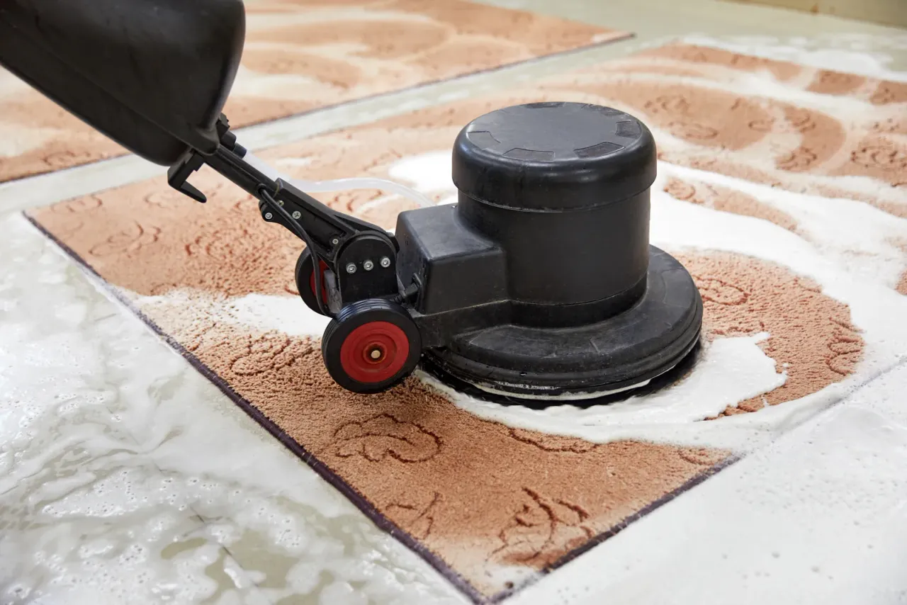 A rotary disc machine scrubbing foam into a terracotta-patterned rug laid on a tile floor, for a page on floor and carpet care in Coachella Valley