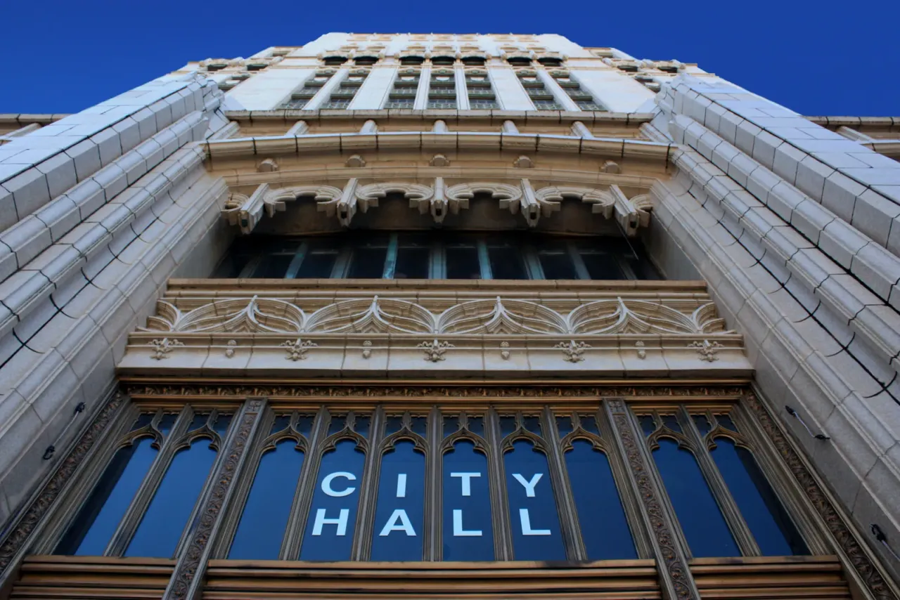 A low-angle view of an ornate stone facade with CITY HALL lettering across its arched windows, accompanying "How Does After-Hours Cleaning Work in Secure Buildings?"