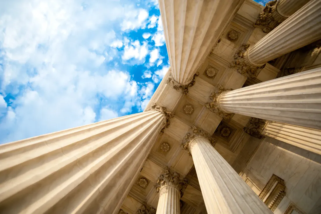 A view straight up between tall fluted stone columns toward a blue sky with clouds, typical of the business properties served by EBS in Downey, CA