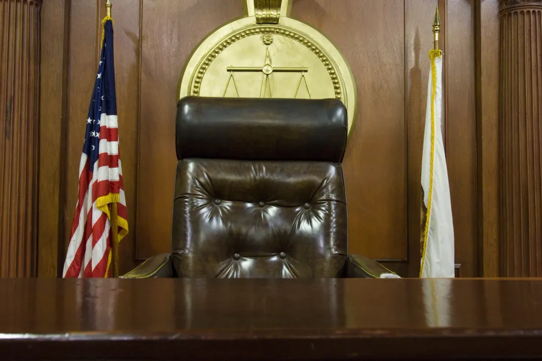 A high-backed leather chair behind a wooden judge's bench, with a US flag and a second flag on either side of a gold seal, an example of office space EBS crews clean after hours in Alhambra, CA