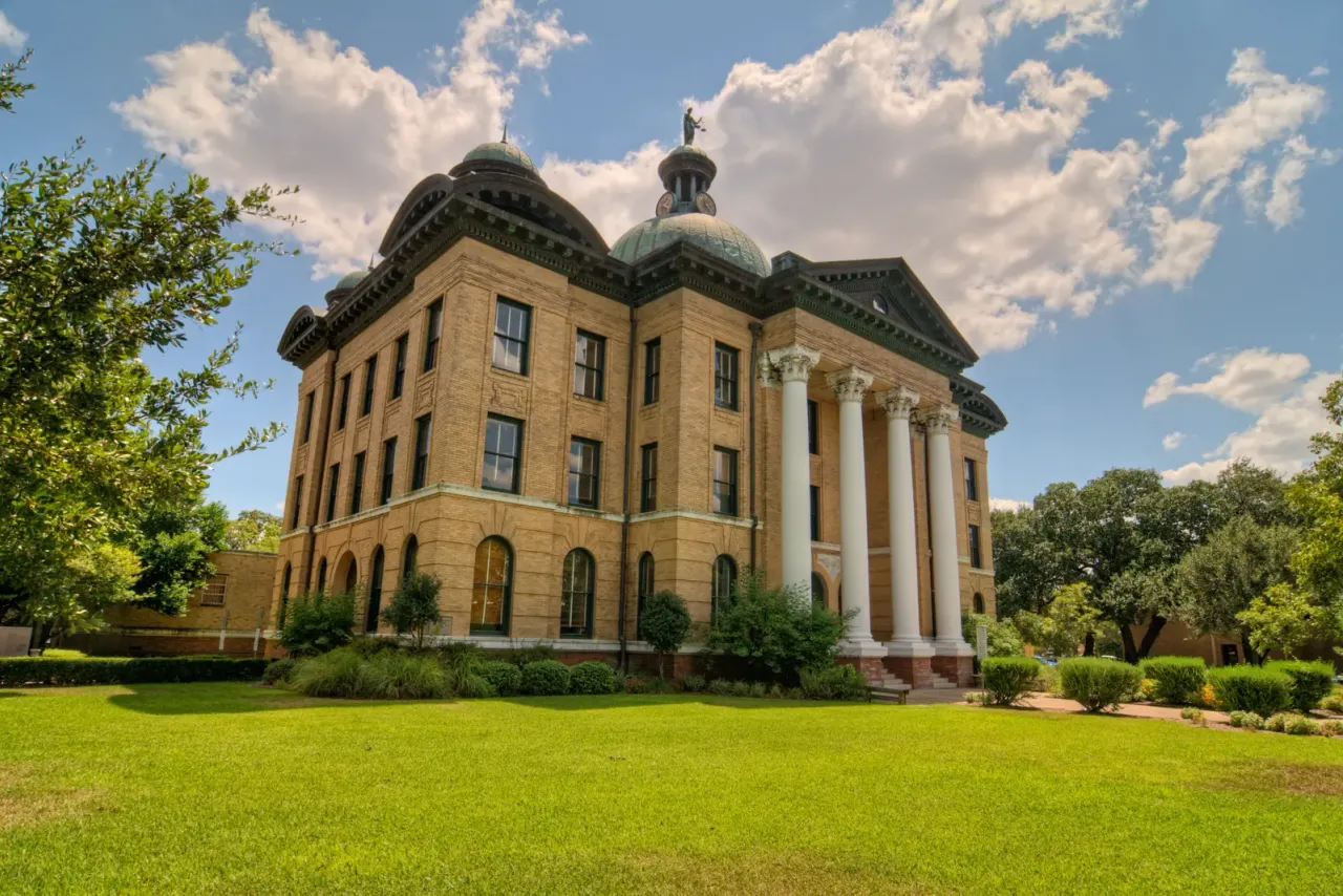 A historic tan brick courthouse with white columns and domed roof towers on a green lawn, typical of the spaces EBS cleans for this industry in Southern California