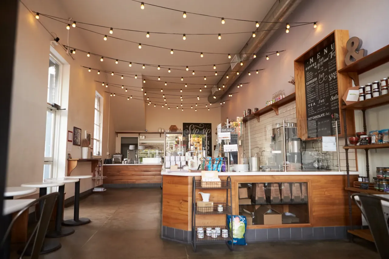 An empty cafe with a wooden service counter, string lights, shelves of goods and a chalkboard menu, typical of the business properties served by EBS in La Quinta, CA