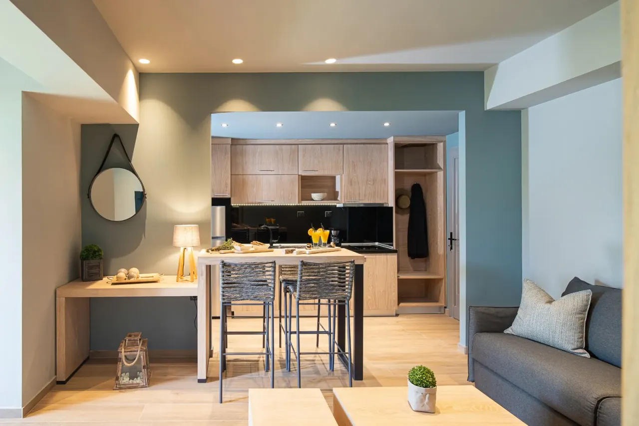 A hotel studio room with a kitchenette, a high table with stools, a grey sofa and a round mirror, illustrating hotel and resort cleaning in Los Angeles County