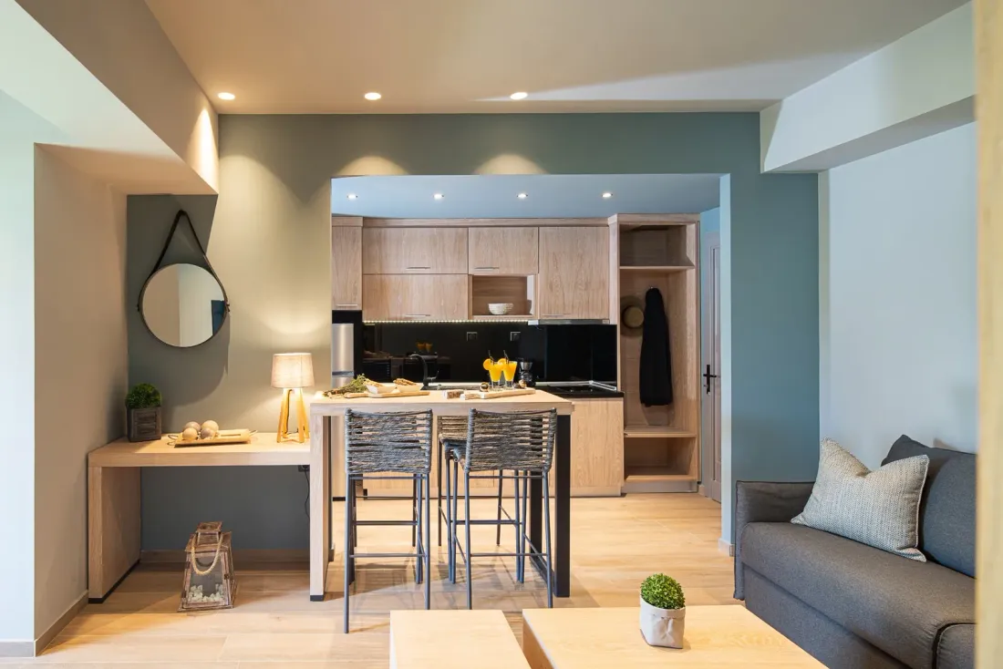 A hotel studio room with a kitchenette, a high table with stools, a grey sofa and a round mirror, typical of buildings served by disinfection services in San Diego County