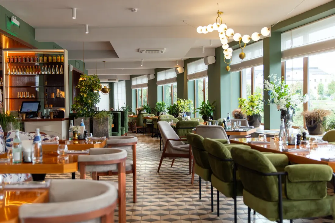 An empty restaurant dining room with green upholstered chairs, wooden tables, a geometric tile floor and tall windows, a setting for commercial cleaning services in Garden Grove, CA