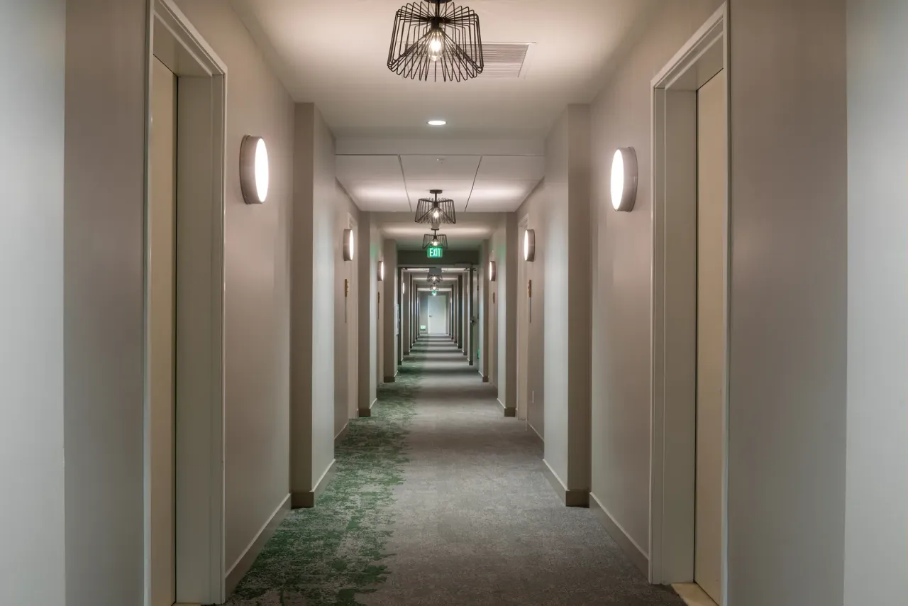 A long hotel corridor with beige walls, patterned carpet, wall sconces and wire pendant lights, a setting for commercial cleaning services in Chula Vista, CA