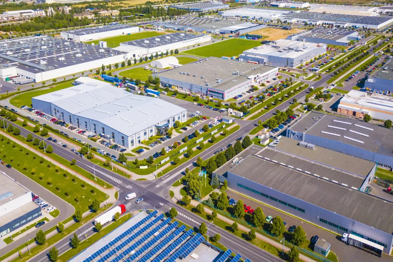 An aerial view of an industrial park with large flat-roofed buildings, parking lots, tree-lined roads and rows of solar panels, the type of commercial property EBS cleans across Fullerton, CA