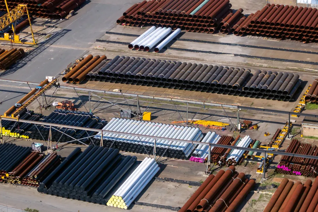 An aerial view of an outdoor yard with stacked steel pipes in rows beside gantry cranes and paved lanes, typical of the distribution and industrial space EBS cleans in Vista, CA