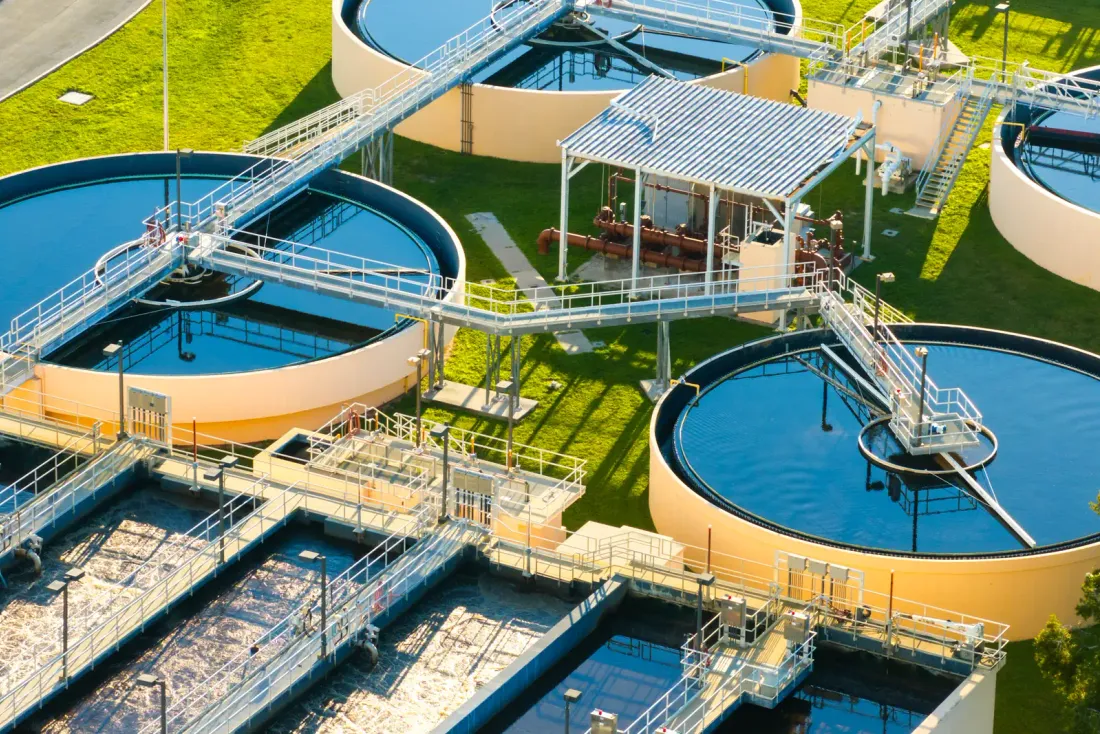 An aerial view of round clarifier tanks, walkways and rectangular basins at a water treatment plant surrounded by lawn, the type of facility covered by warehouse cleaning in Paramount, CA