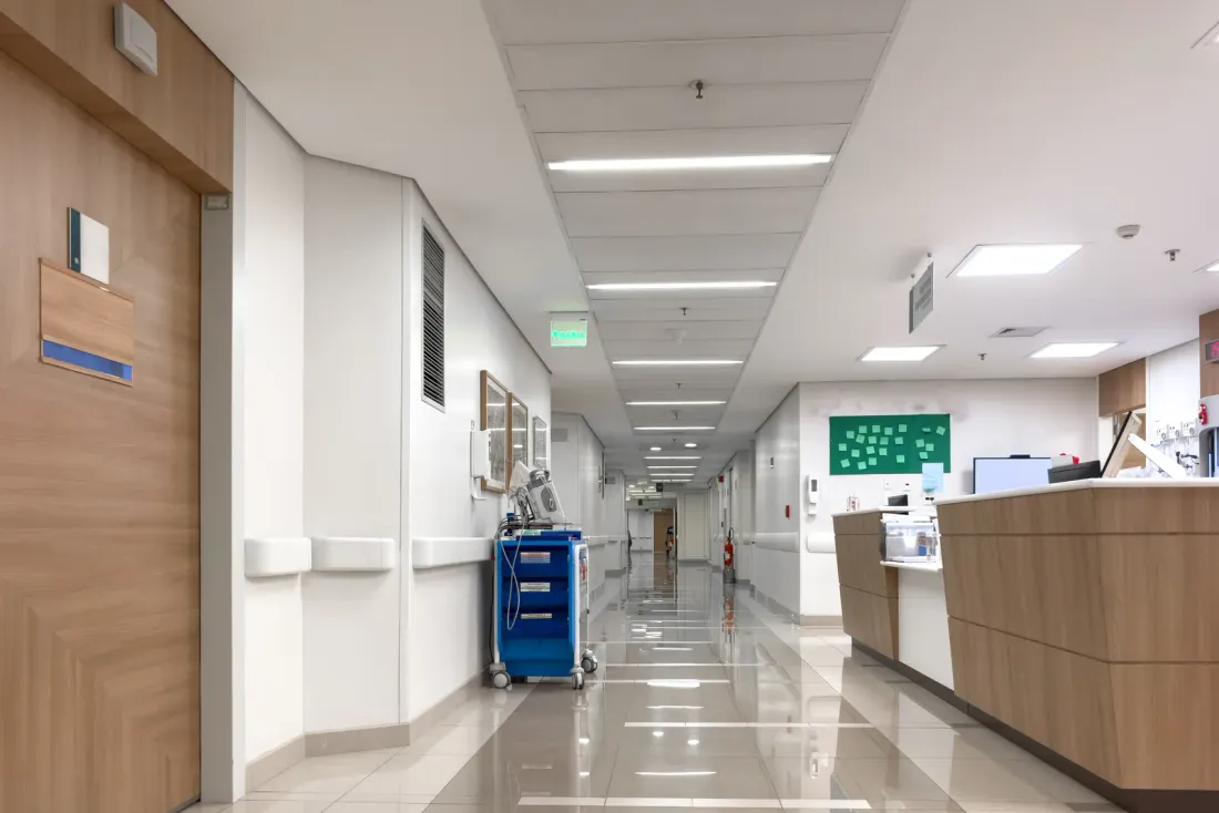 A hospital corridor with wood-panelled doors, a nurses' station counter, a supply cart and a polished floor under ceiling lights, accompanying "What Does USP 797 Require for Compounding Room Cleaning?"