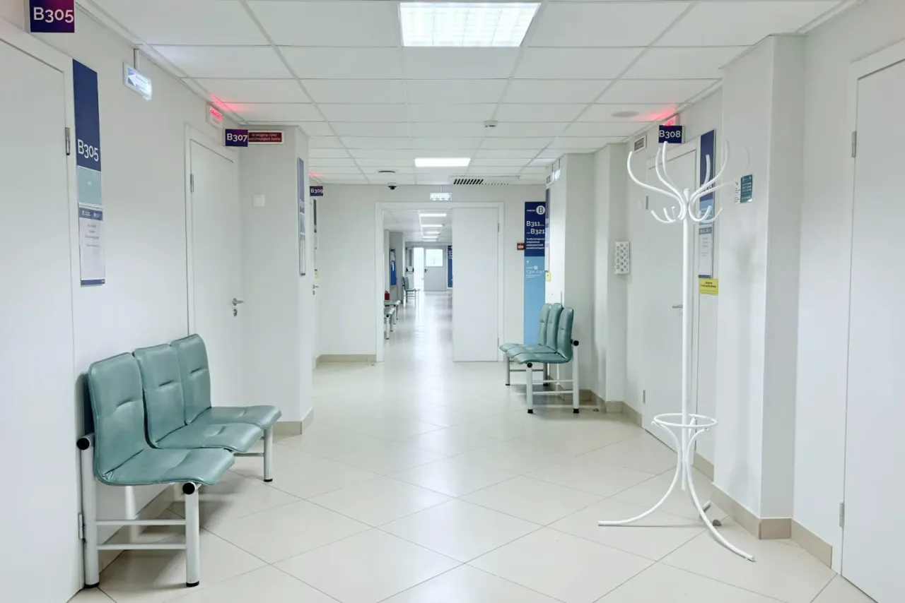 A bright hospital corridor with a white tile floor, teal waiting chairs, a white coat stand and numbered doors, the kind of healthcare setting EBS cleans with EPA-registered disinfectants in Irvine, CA