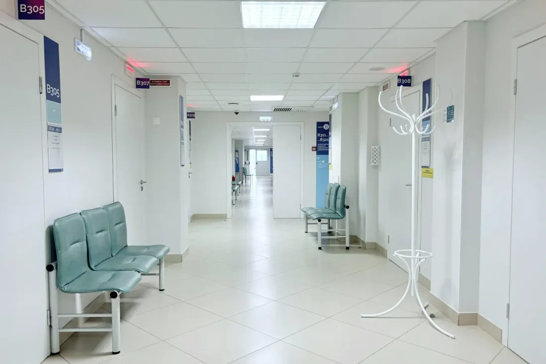 A bright hospital corridor with a white tile floor, teal waiting chairs, a white coat stand and numbered doors, a setting for commercial cleaning services in Montclair, CA