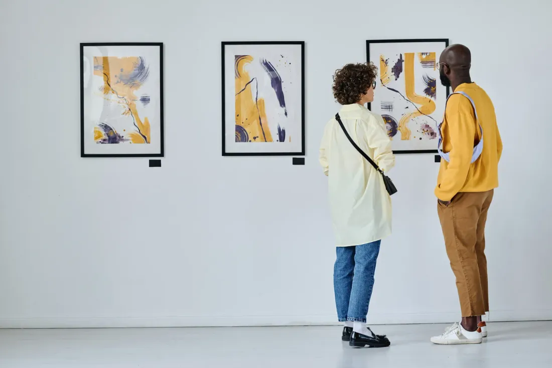 Two visitors standing close to framed abstract prints on a white gallery wall, typical of the business properties served by EBS in Costa Mesa, CA
