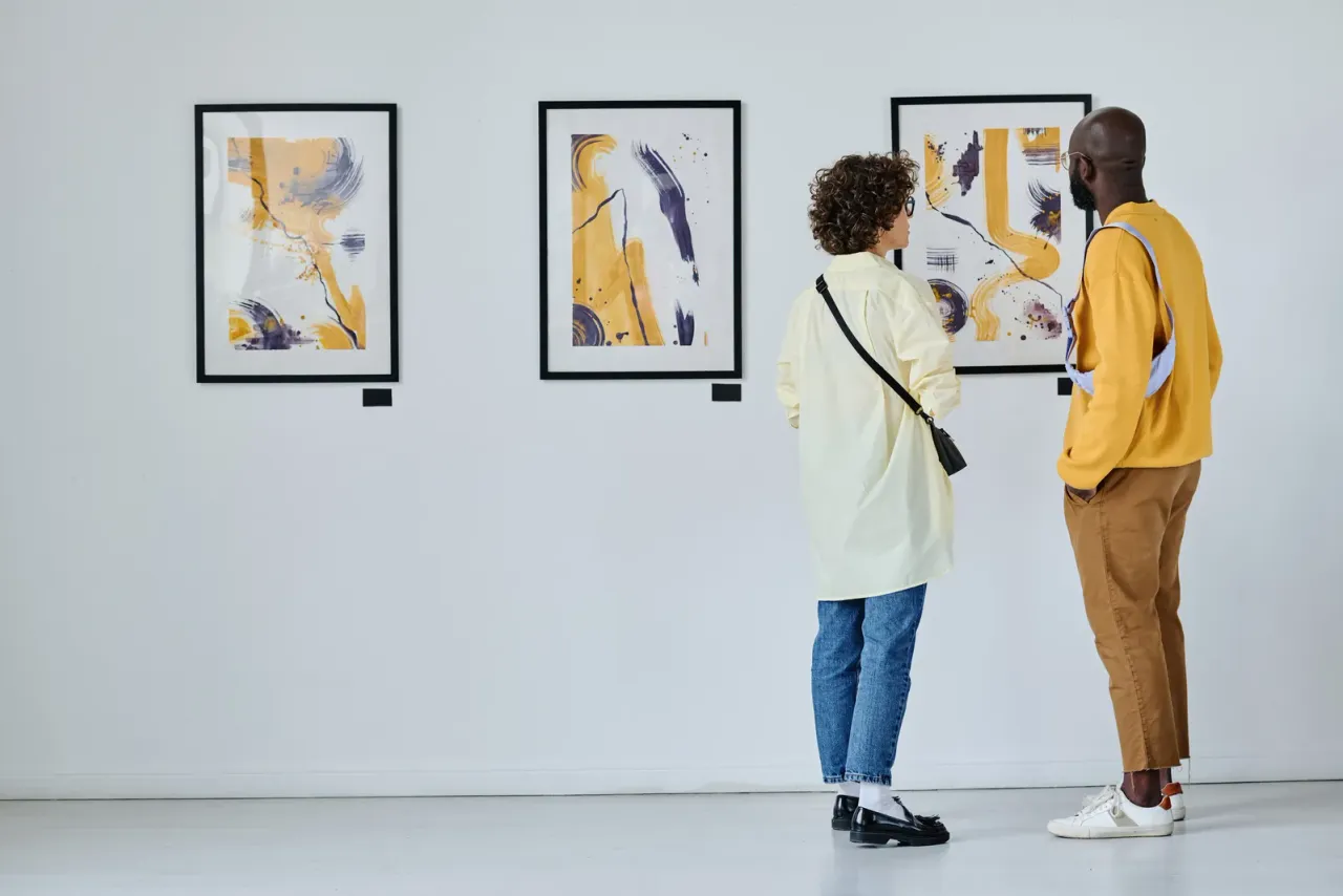 Two visitors standing close to framed abstract prints on a white gallery wall, typical of the facilities covered by museum and gallery cleaning in San Bernardino County