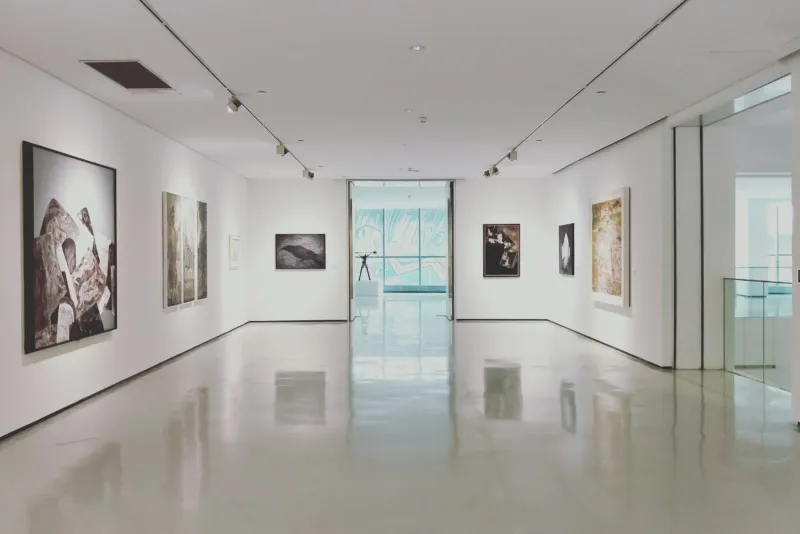 A bright modern gallery with white walls, a polished floor and framed works