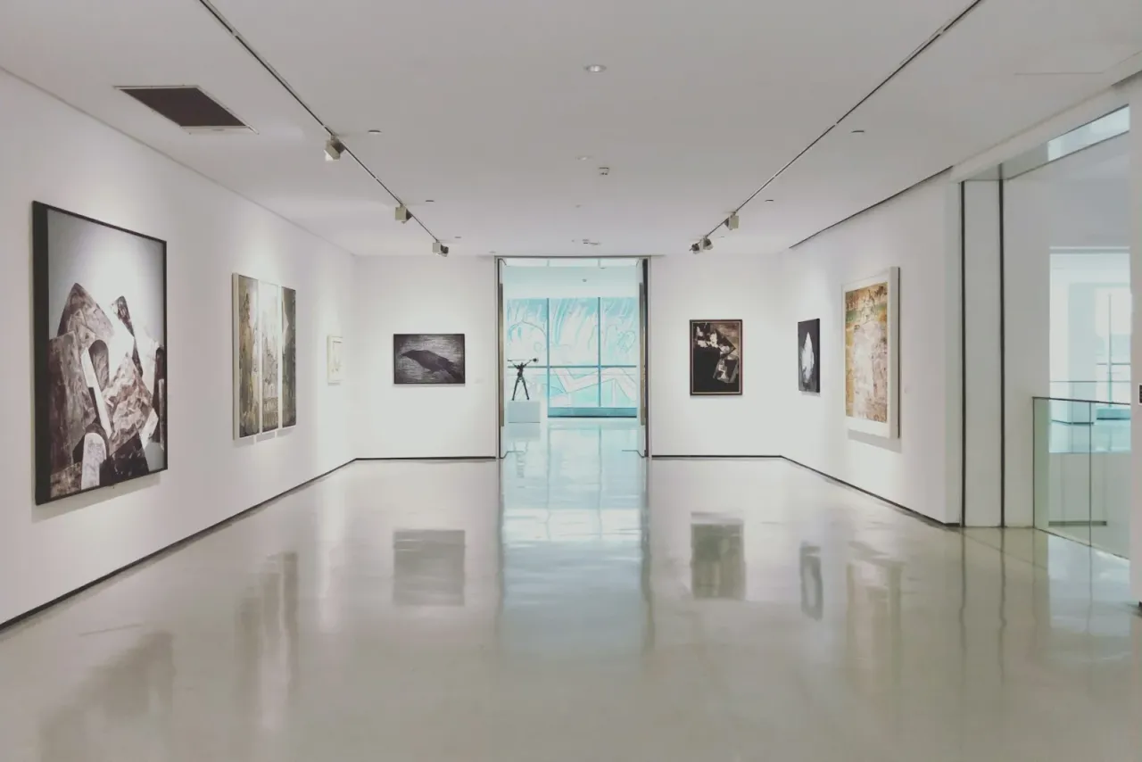 An empty white gallery with framed pictures on the walls, track lighting and a polished floor leading to a glass doorway, illustrating museum and gallery cleaning in Riverside County