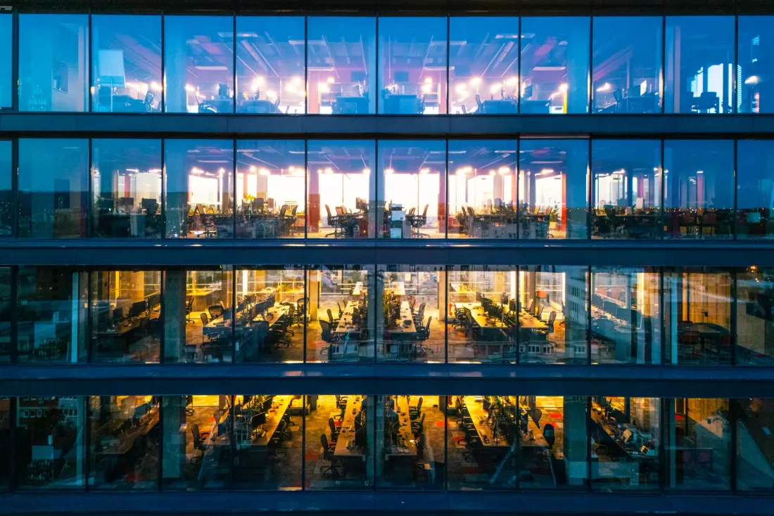 A glass office facade at dusk with lit, empty open-plan floors visible through the windows, typical of the business properties served by EBS in Chatsworth, CA