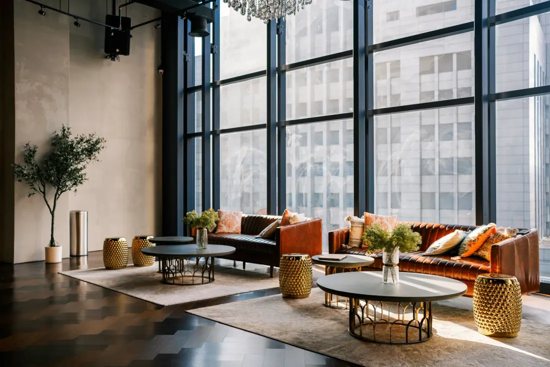 A lobby lounge with brown leather sofas, round coffee tables, potted trees and tall black-framed windows, the kind of workspace covered by office cleaning in Murrieta, CA