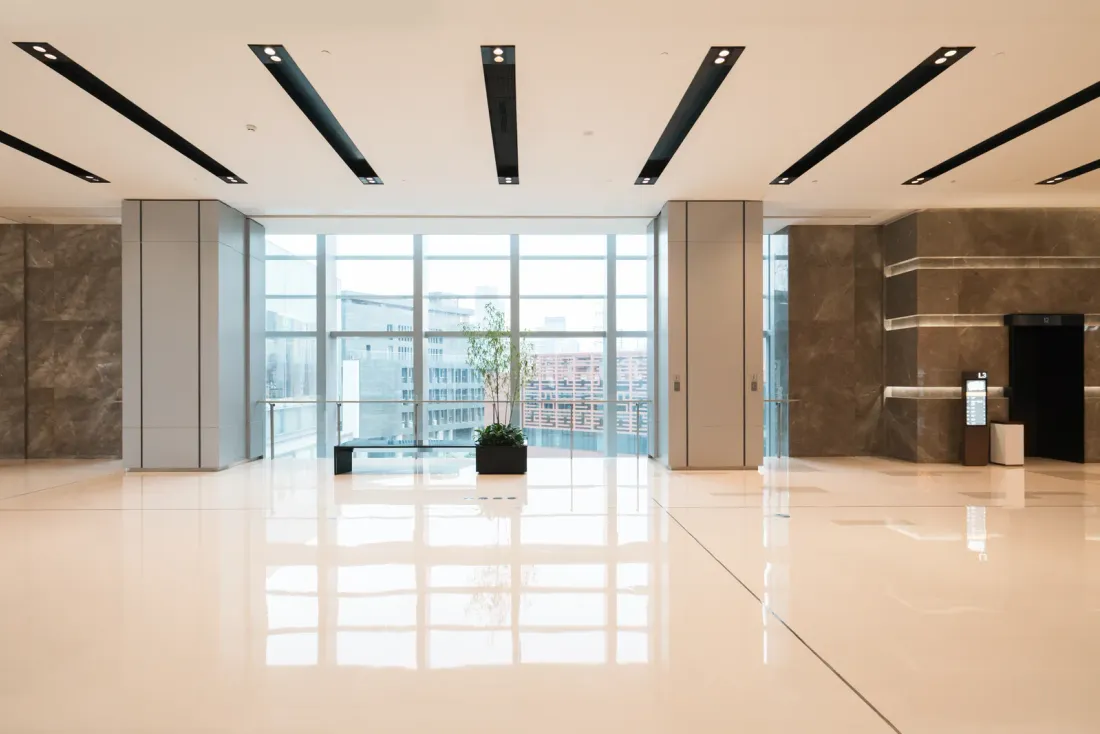 An empty lobby with polished cream floor tiles, stone-clad walls, a small potted plant and floor-to-ceiling windows, typical of the facilities covered by office building cleaning in Orange County
