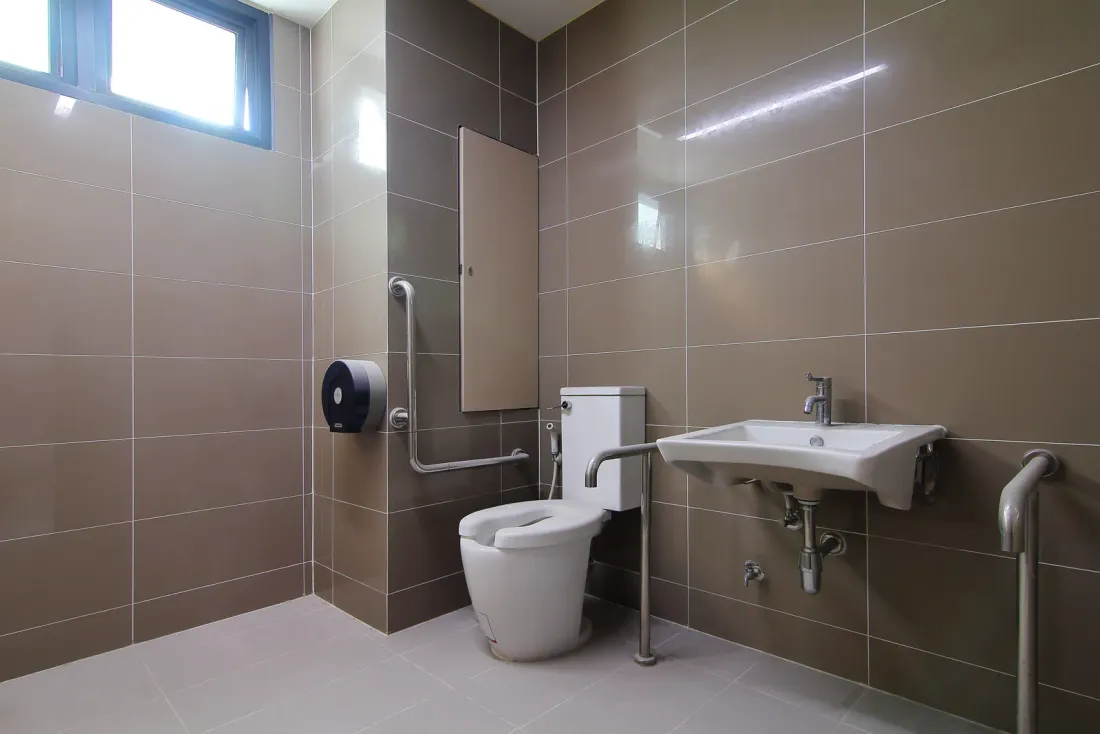An accessible restroom with taupe wall tiles, grab bars, a wall-mounted sink and a toilet, the kind of space EBS janitorial crews maintain in Baldwin Park, CA