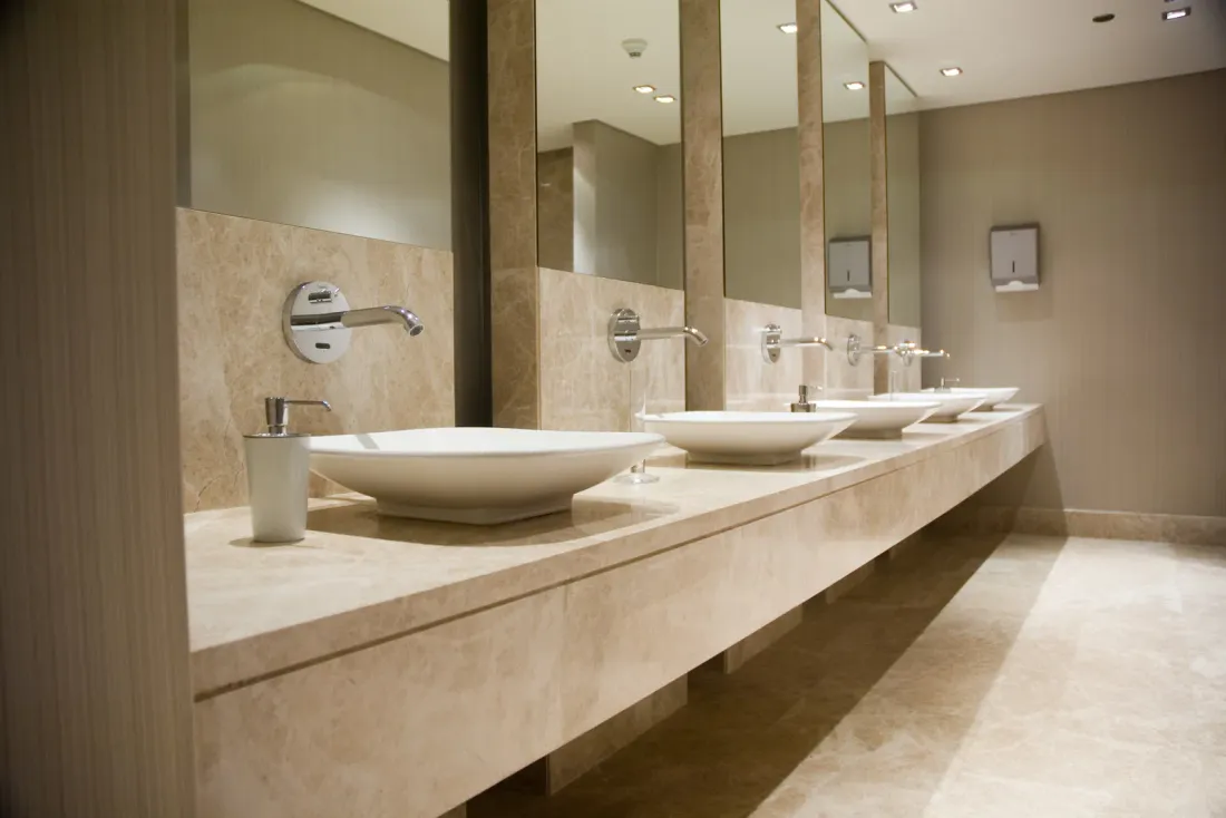 A row of round vessel sinks with wall-mounted faucets on a beige stone counter under long mirrors, an example of the facilities EBS cleans on a set schedule in Dana Point, CA