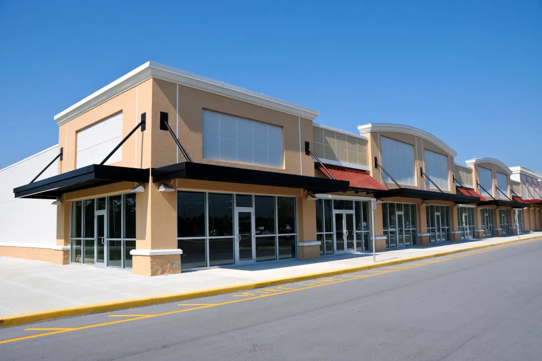 A beige single-storey retail building with empty glass storefronts and black awnings along a quiet road, a setting for commercial cleaning services in Eastvale, CA