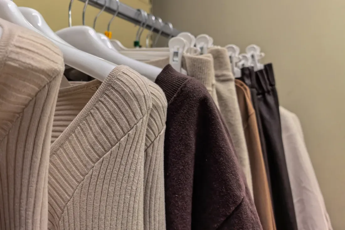 Neutral-toned knit sweaters and trousers hanging on a clothing rack, a common area that day porter service keeps ready in Cerritos, CA