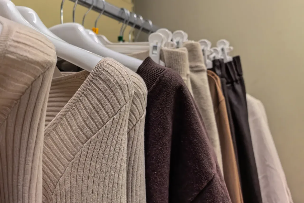 Neutral-toned knit sweaters and trousers hanging on a clothing rack, an example of the facilities covered by retail store cleaning services