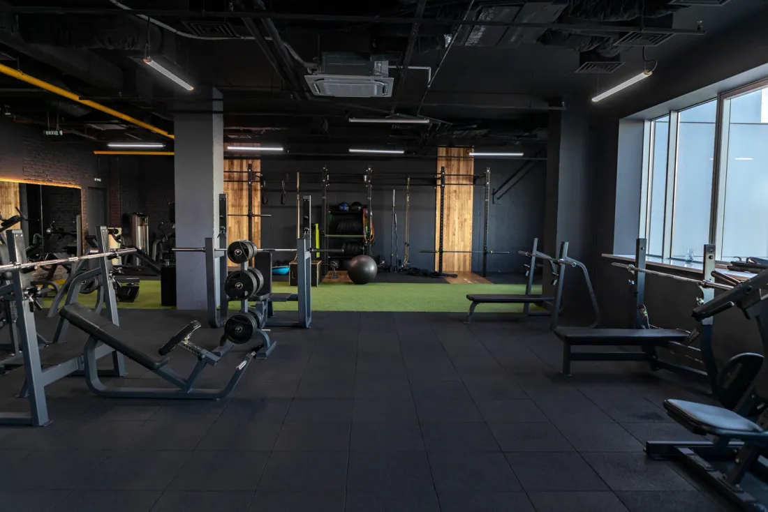 An empty gym with strength machines and benches on black rubber flooring under exposed ductwork, typical of the business properties served by EBS in Hollywood, CA