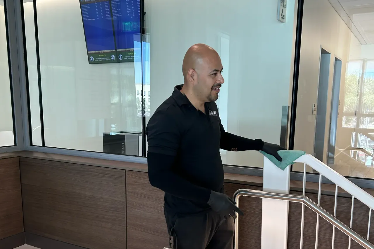 An EBS team member in a uniform with the EBS logo, wearing gloves and wiping down a stair railing in a lobby