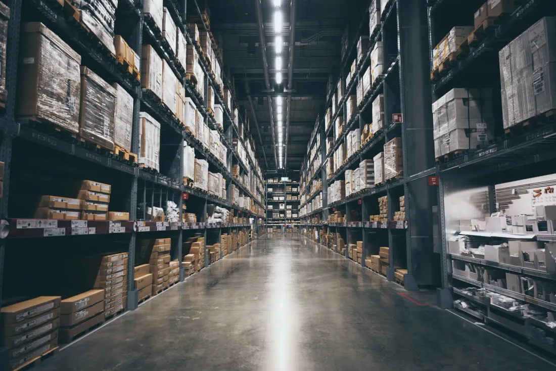 A long, dim warehouse aisle between tall shelving stocked with boxes, with a glossy concrete floor, typical of the business properties served by EBS in Bell, CA